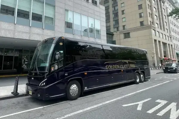 Black MCI motor coach in gold Golden Class Limo livery, parked at a Manhattan kerb