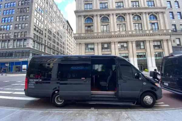 Black 14-passenger Mercedes Sprinter van with its side door open on a Manhattan street, Astoria Transport Corp lettering on the rear panel
