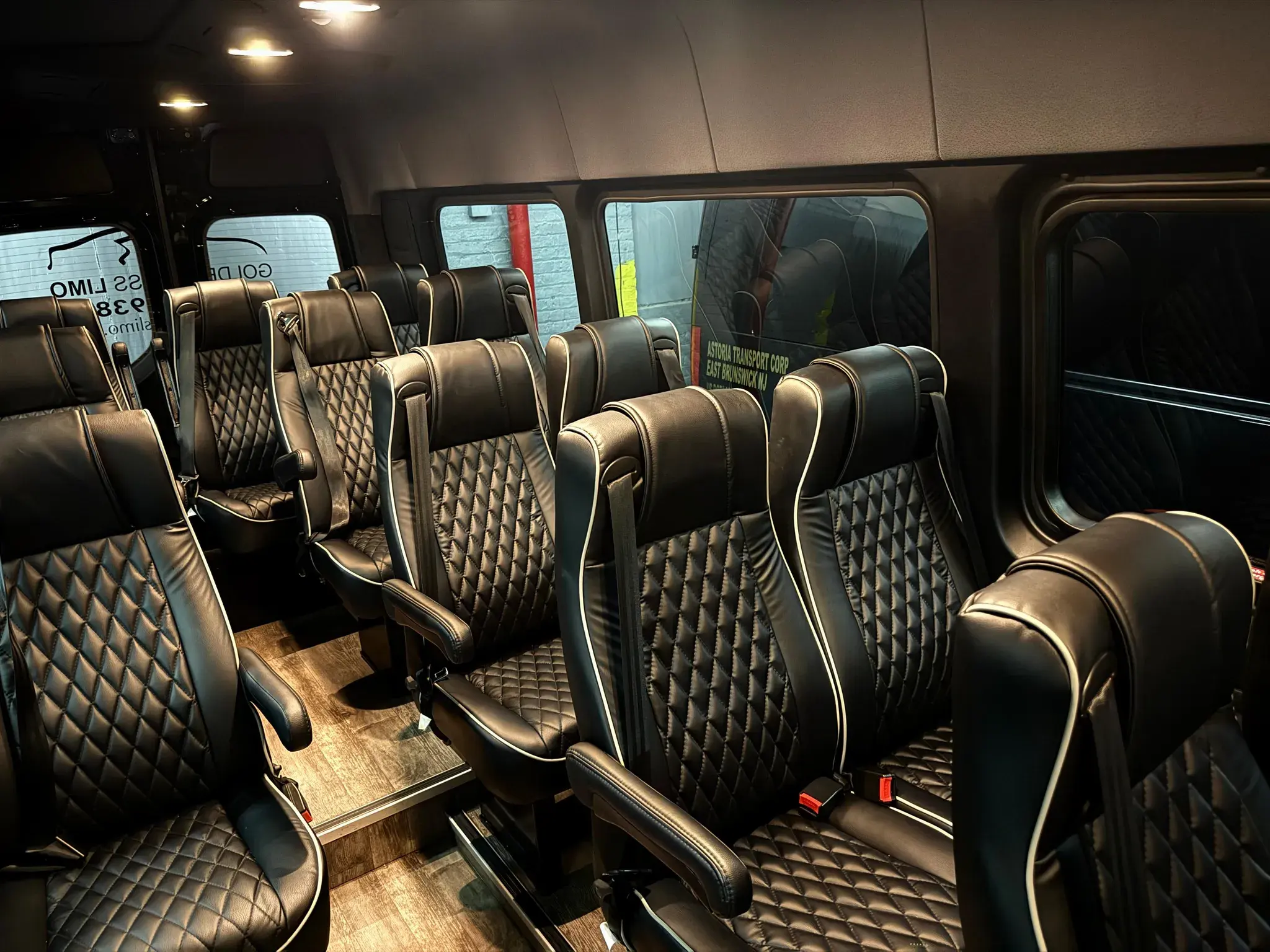 Forward-facing quilted leather rows inside the 14-passenger Standard Sprinter, with the Astoria Transport Corp lettering and the Golden Class Limo wordmark visible through the glass