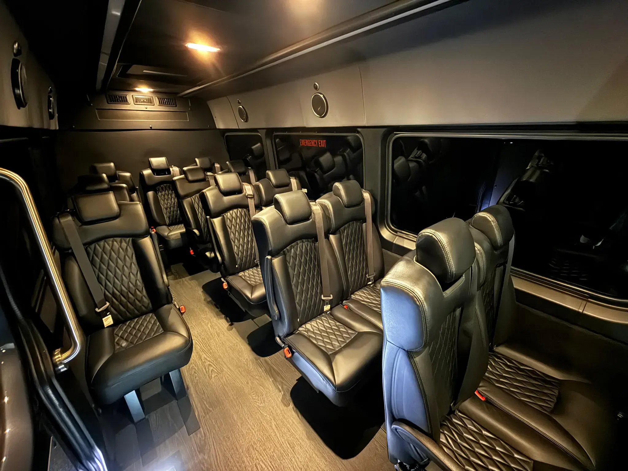 Quilted black leather rows and a hardwood floor running the length of a 14-passenger Sprinter cabin