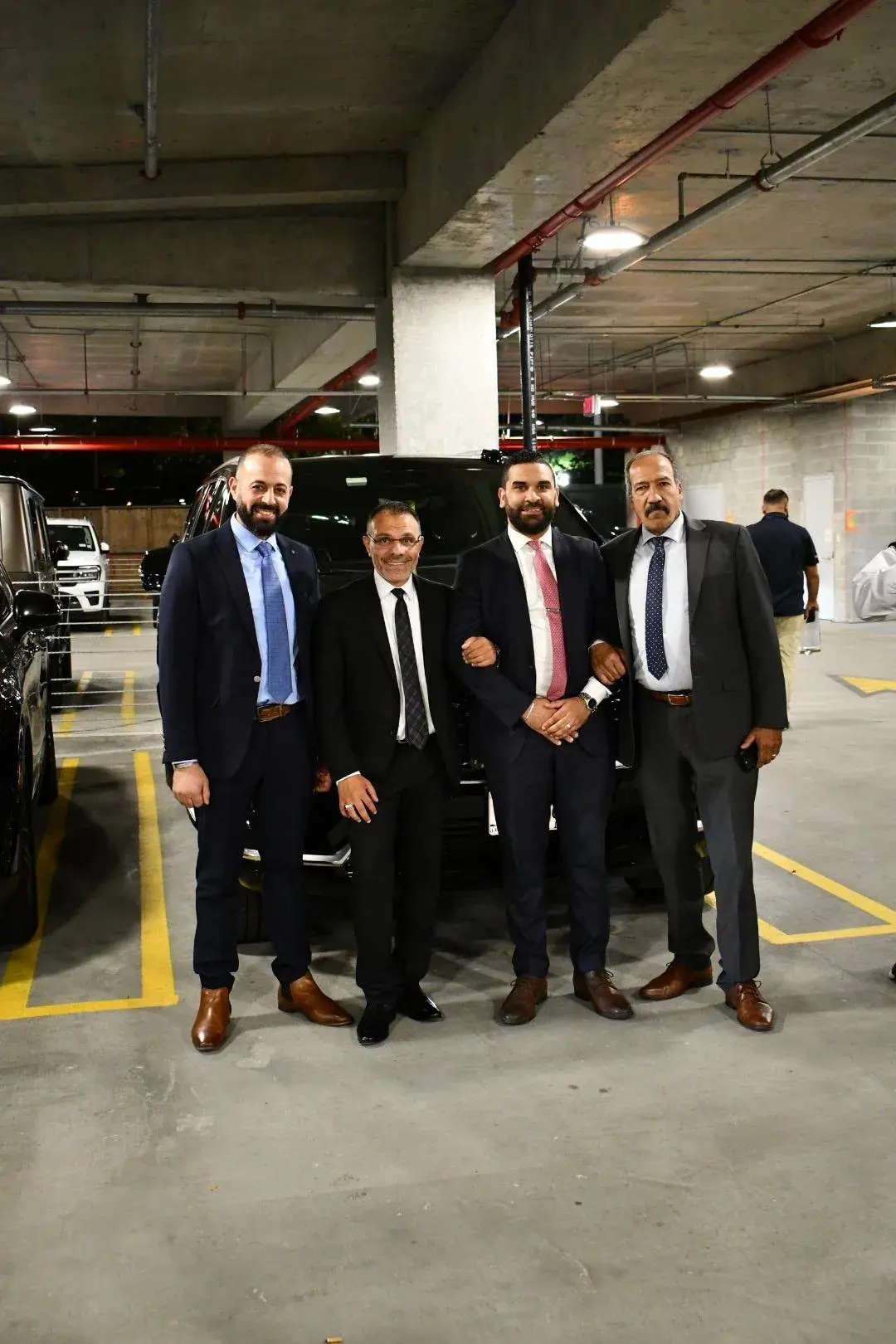 Four Golden Class Limo staff in suits in front of a black SUV in a parking garage